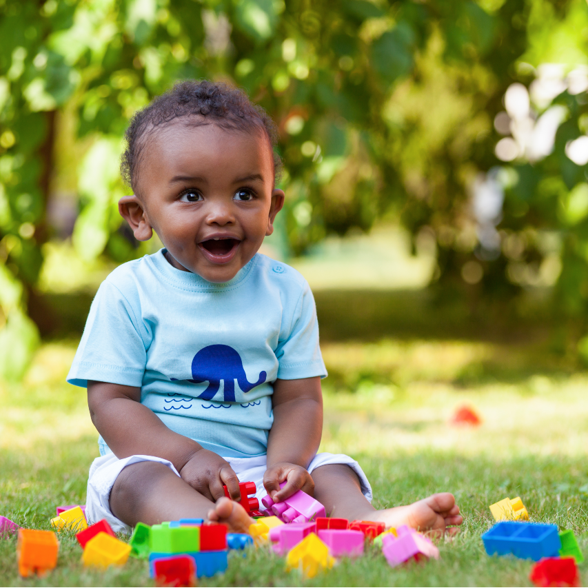 Laughing little baby boy playing with bricks on the grass