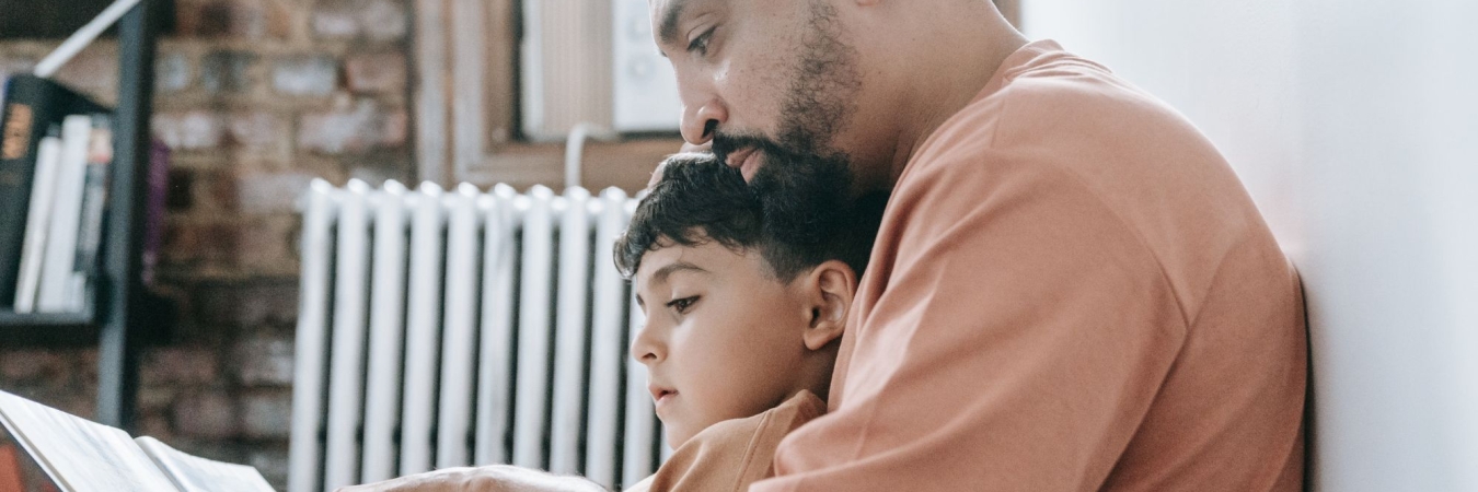 A father and son sitting on the floor reading a book together pointing at the words