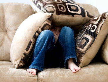 child in jeans hiding under cushions on the sofa 