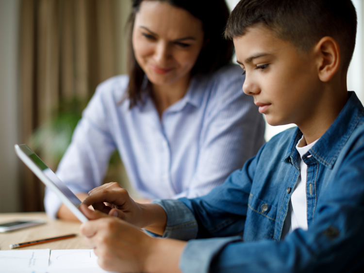 mum in background smiling gently at boy using a tablet