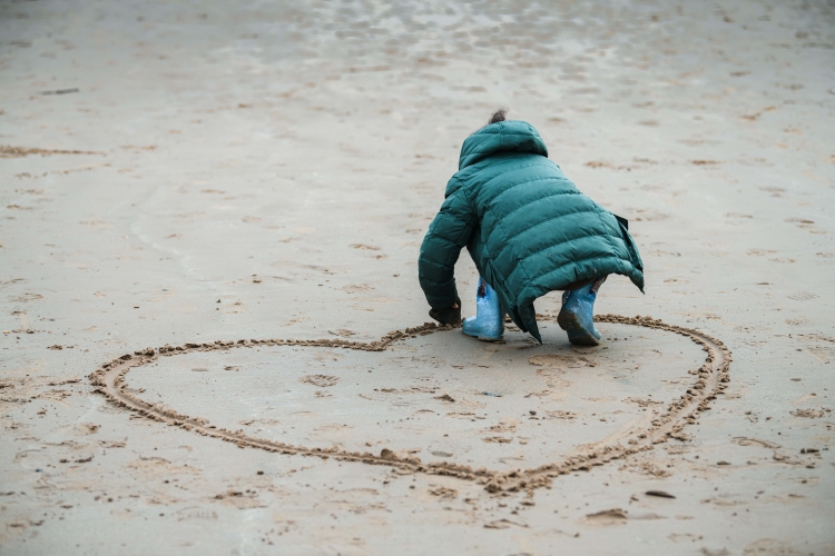 Child draws heart in sand