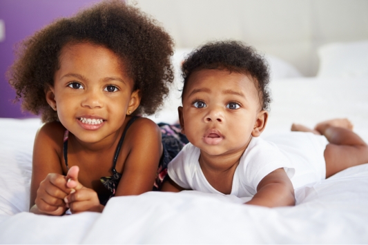 Little girl and baby brother laying on their fronts looking at the camera