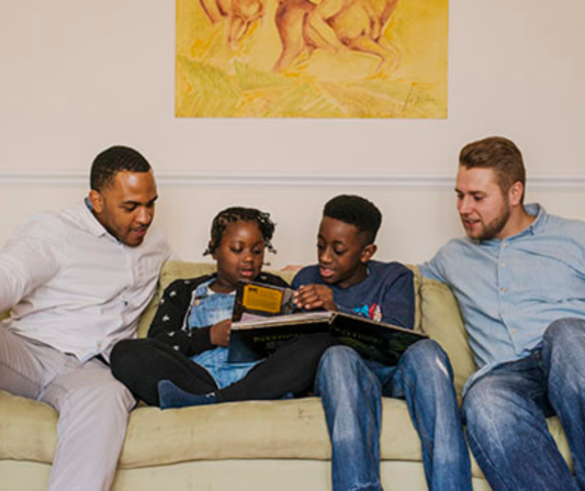 two dads sitting on sofa watching their two older reading