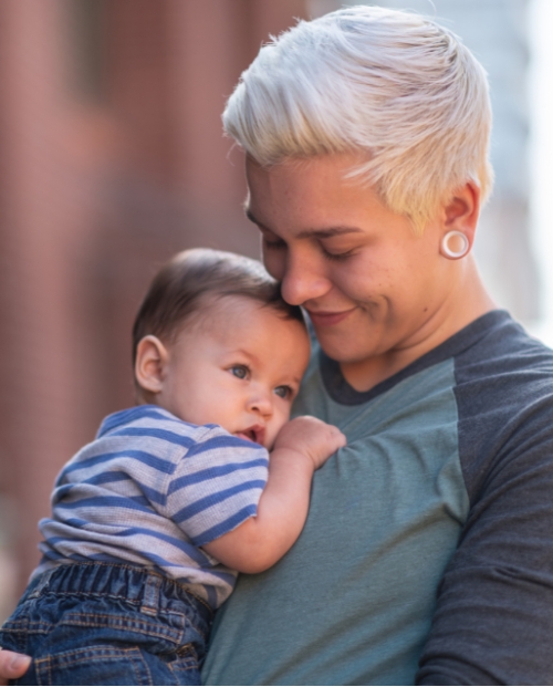A non binary person holding their baby 